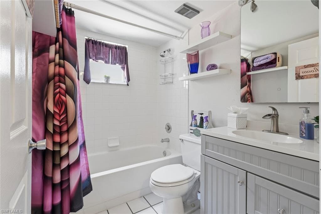 Bathroom featuring white tile flooring, a white bathtub, and a vanity with a light gray beadboard finish and a white countertop