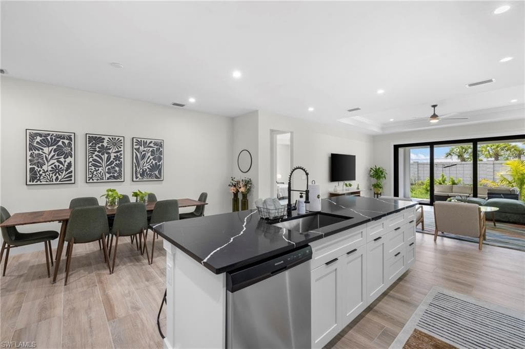 Open-concept living space featuring a central kitchen island with a dark countertop and integrated sink, stainless steel dishwasher, wood-finish flooring, and expansive sliding glass doors