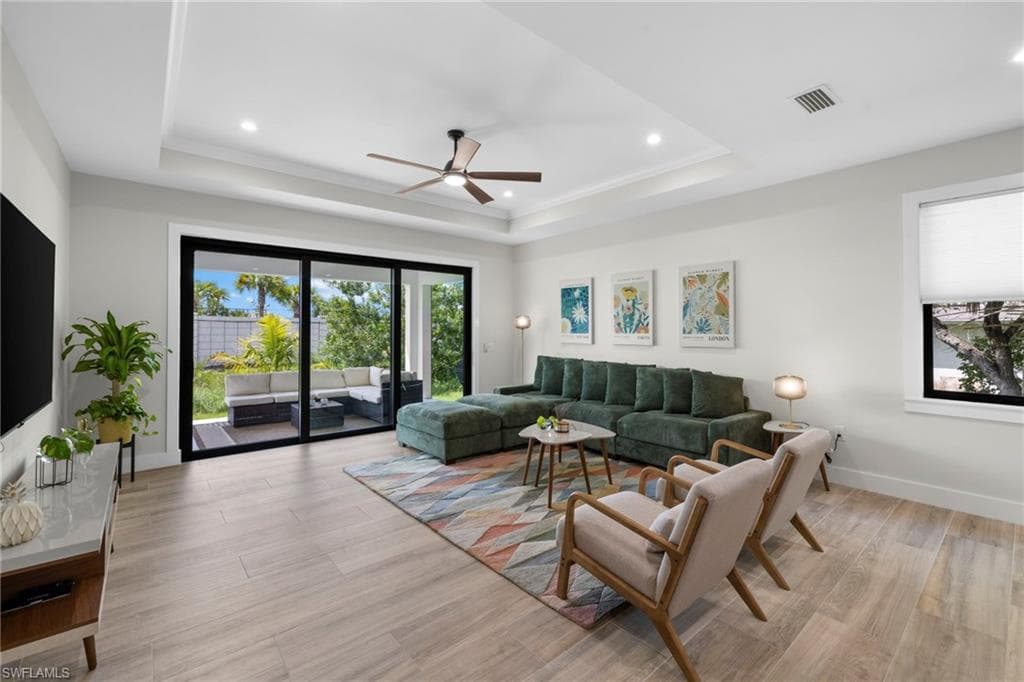 Open-concept living area featuring wood-finish flooring, a tray ceiling with recessed lighting, and a modern ceiling fan