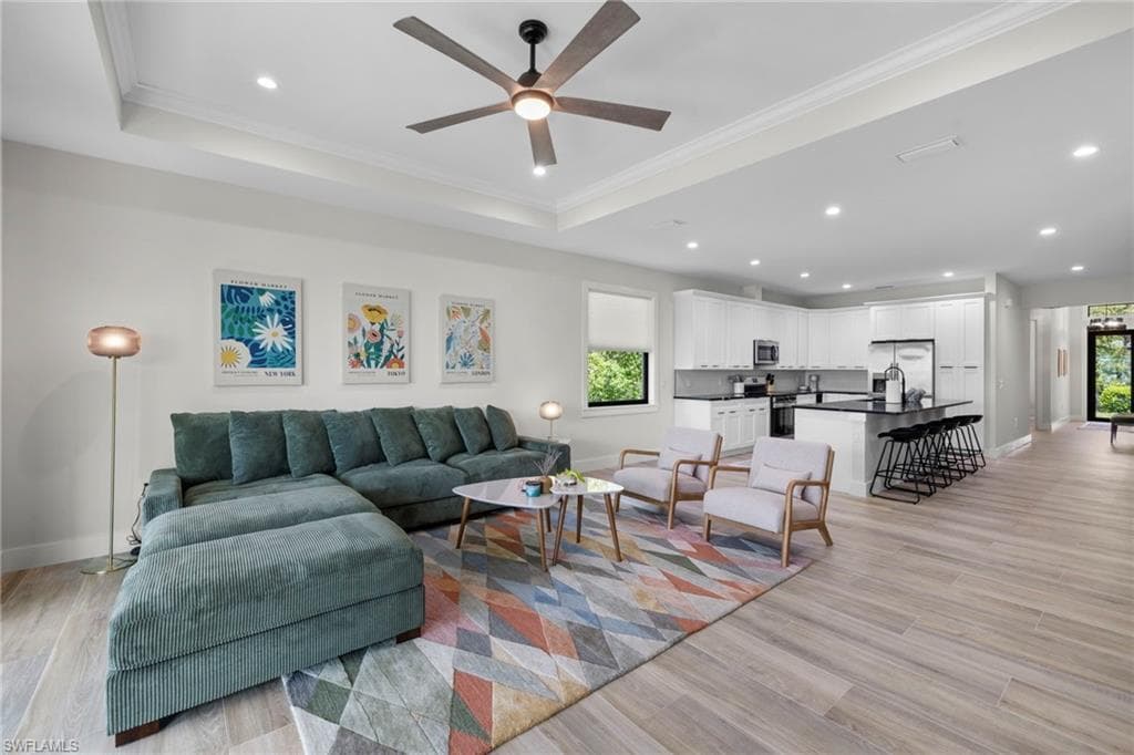 Open-concept interior featuring wood-finish flooring, a tray ceiling with a ceiling fan, recessed lighting, white cabinetry, and a dark kitchen island with seating