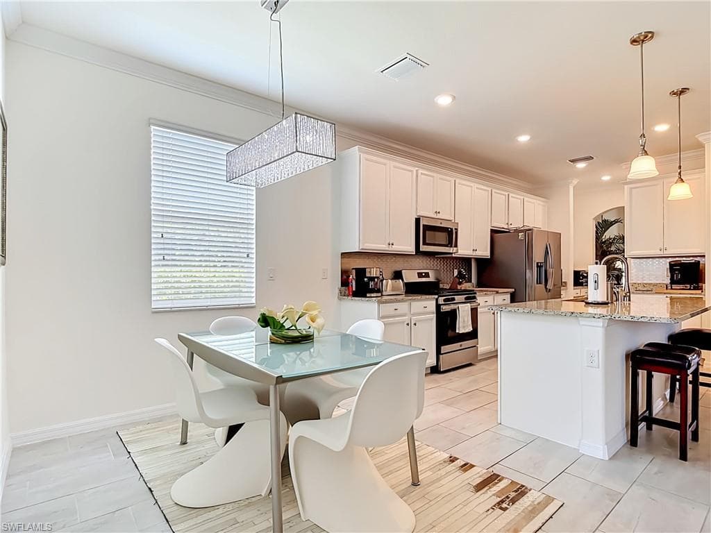 Open-concept kitchen and dining area featuring white cabinetry, stainless steel appliances, tile flooring and a breakfast bar with Granite countertops