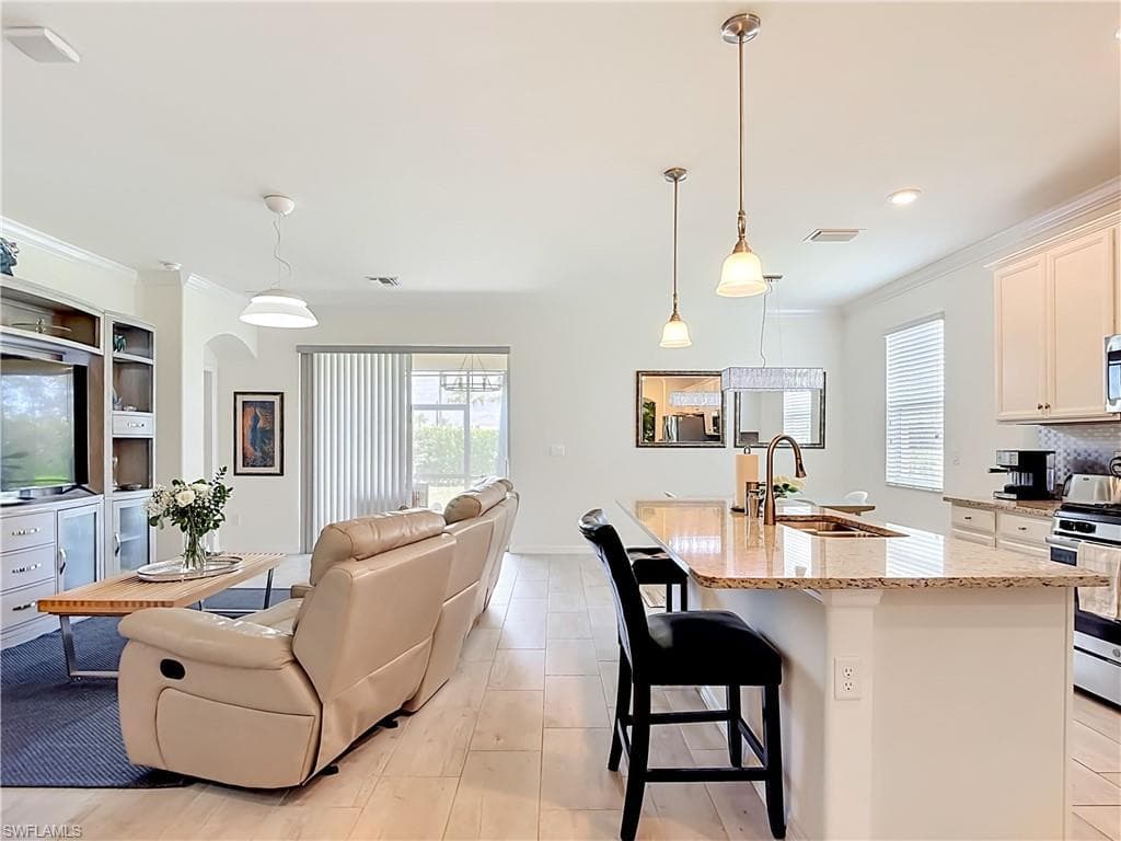 Expansive open-concept living area featuring wood-finish flooring, a kitchen island with stone countertop, pendant lighting, and white cabinetry