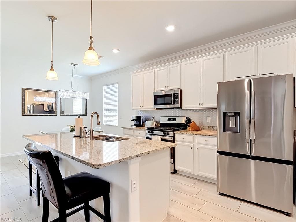 Kitchen featuring a central island with a double basin sink, granite-finish countertops, stainless steel appliances, white cabinetry, and light-toned tile flooring
