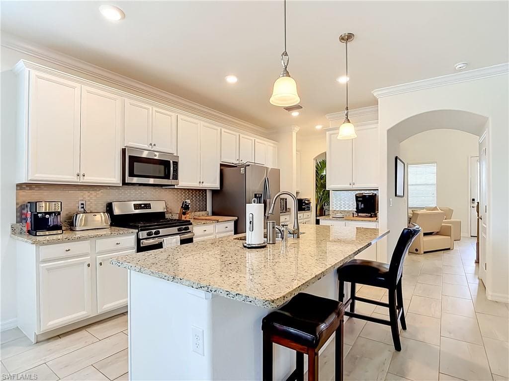 Gourmet kitchen featuring a central island with bar seating, granite countertops, white cabinetry, stainless steel appliances, and tile flooring
