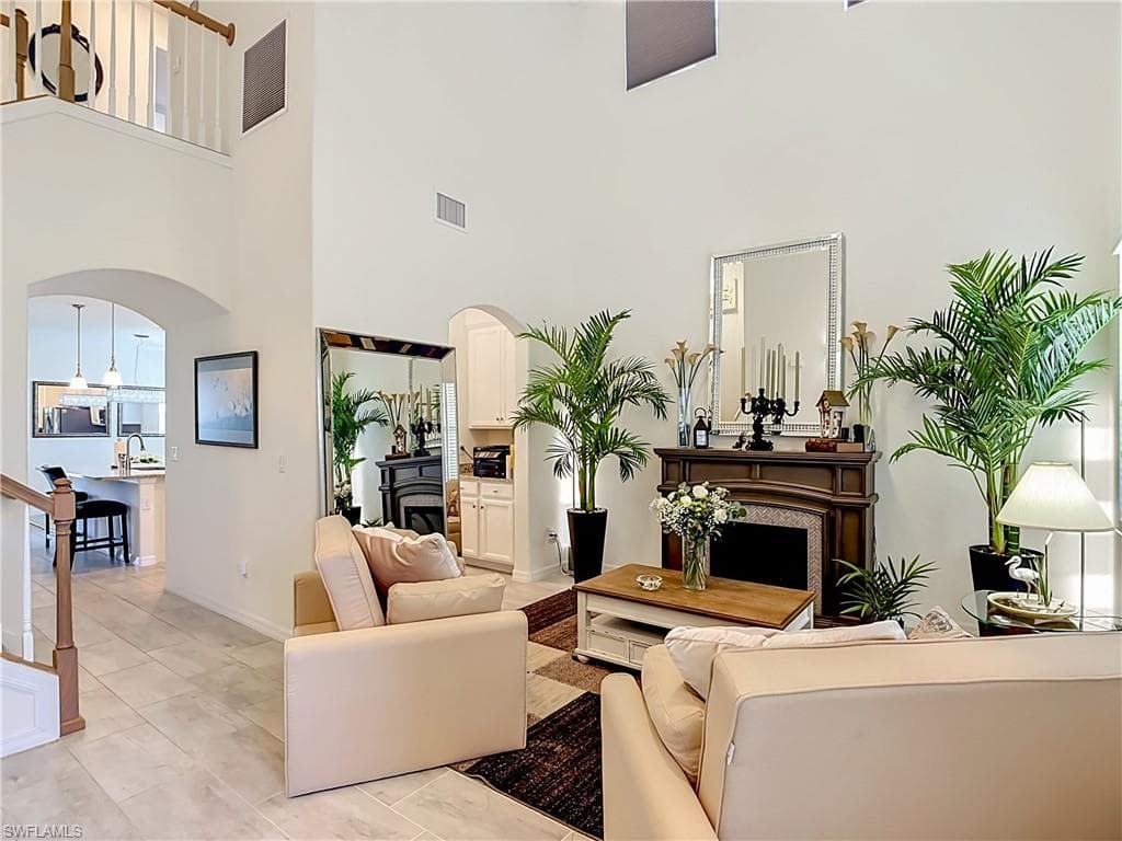 Two-story living area featuring a fireplace with a detailed mantel, high ceilings, arched doorways, and light tile flooring