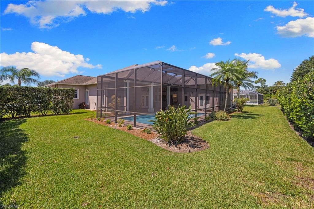 Expansive backyard featuring a screened-in pool enclosure, mature palm trees, and established perimeter hedges