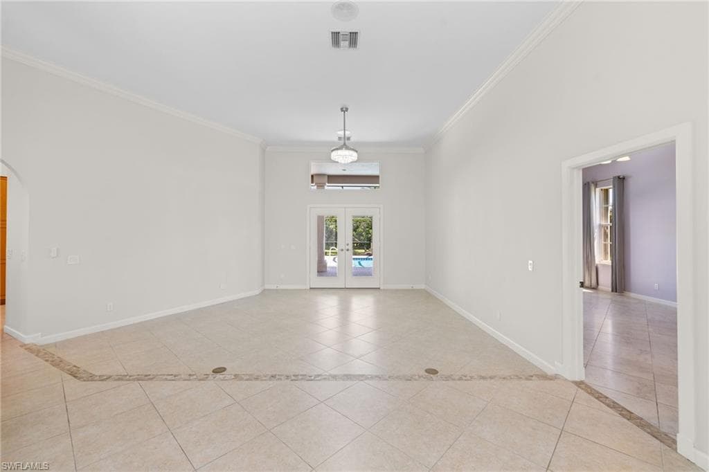 Spacious living area featuring neutral tile flooring, high ceilings, crown molding, and double French doors leading to an outdoor area