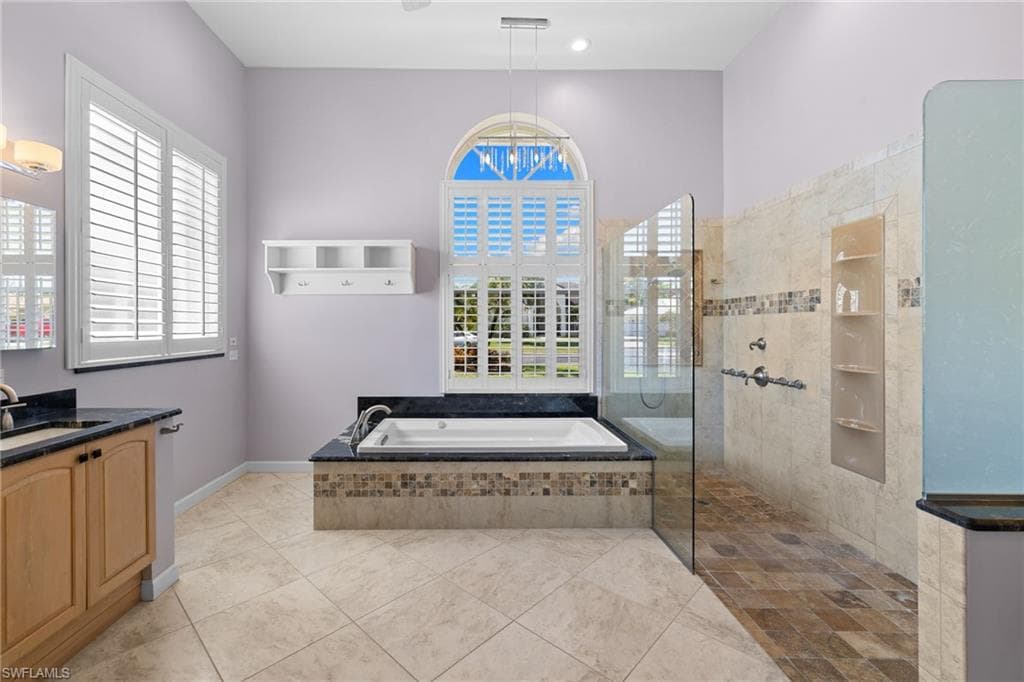 Primary bathroom #1 featuring an integrated soaking tub with stone surround, a dual vanity with a granite countertop, and tiled flooring