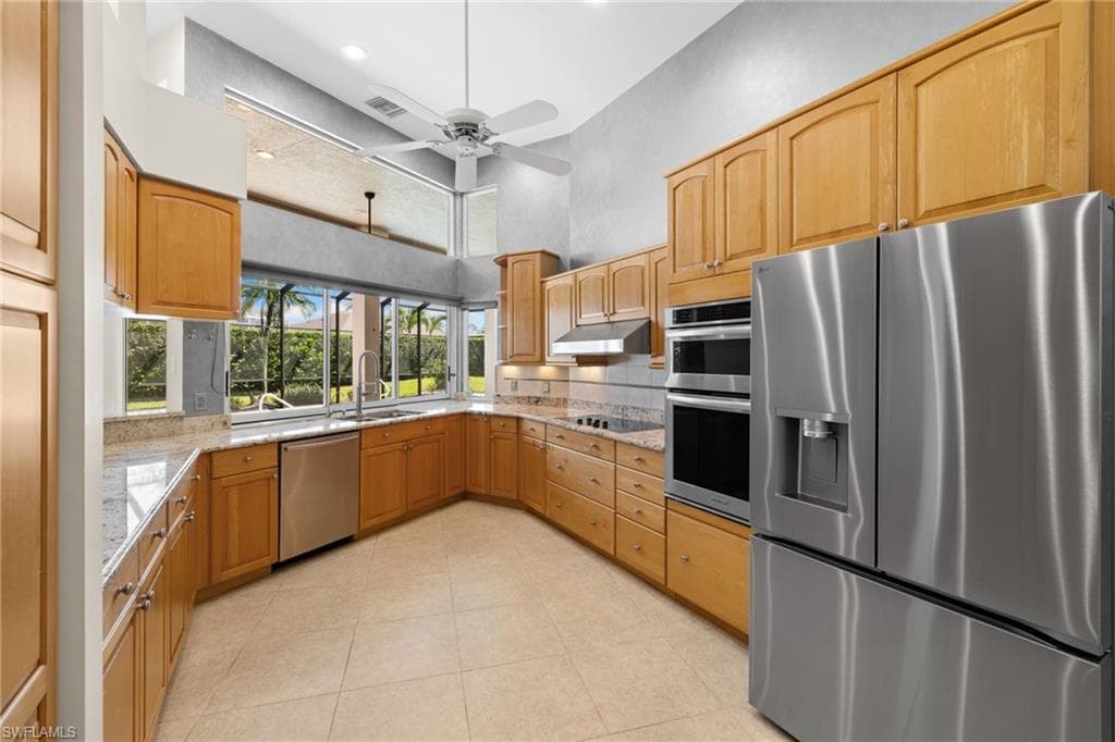 Spacious kitchen featuring light wood cabinetry, stone-finish countertops, stainless steel appliances, and a ceiling fan