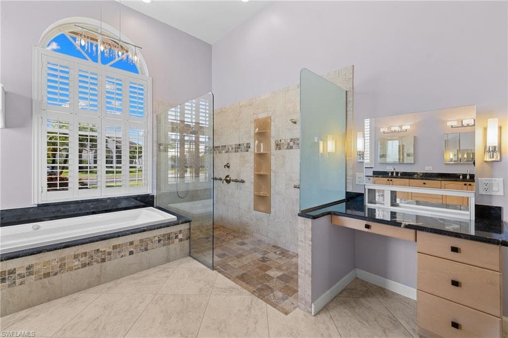 Primary bathroom #1 featuring a built-in soaking tub with mosaic tile surround, a separate walk-in shower with glass enclosure and tiled niche, dual vanity with black countertops, and plantation-shuttered windows