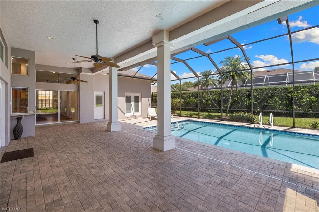 Expansive screened lanai featuring a swimming pool, textured paver patio, and ceiling fans