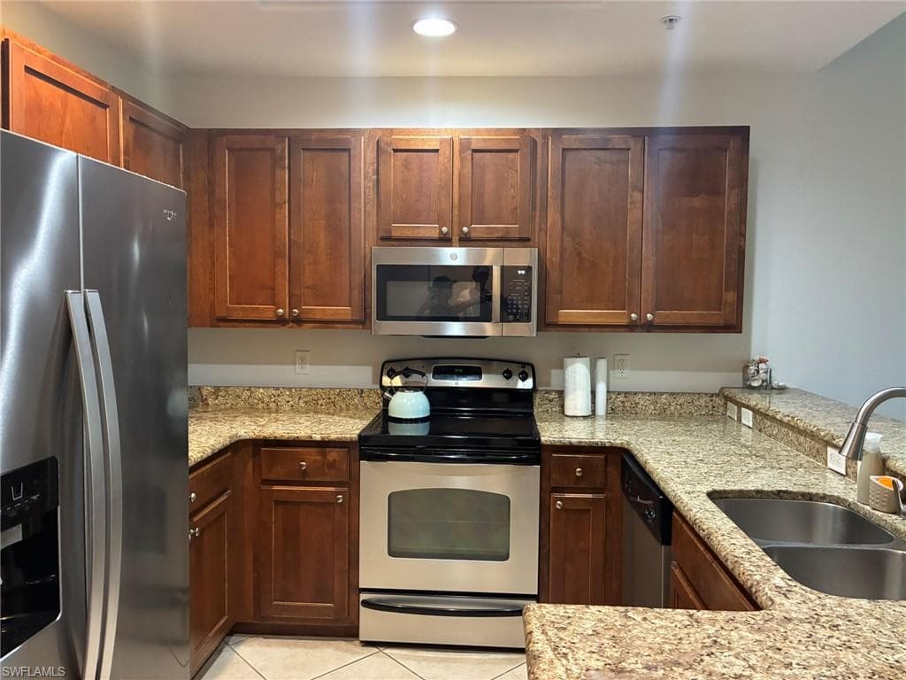 U-shaped kitchen featuring wood cabinetry, speckled countertops, and stainless steel appliances including a refrigerator, range, microwave, and dishwasher