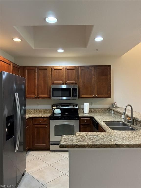 Kitchen featuring wood cabinetry, stainless steel appliances, speckled countertops, and tile flooring