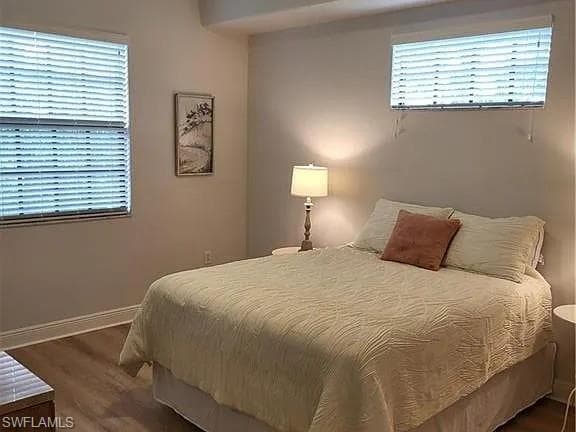 Bedroom featuring wood-finish flooring, two windows with horizontal blinds, and neutral wall tones