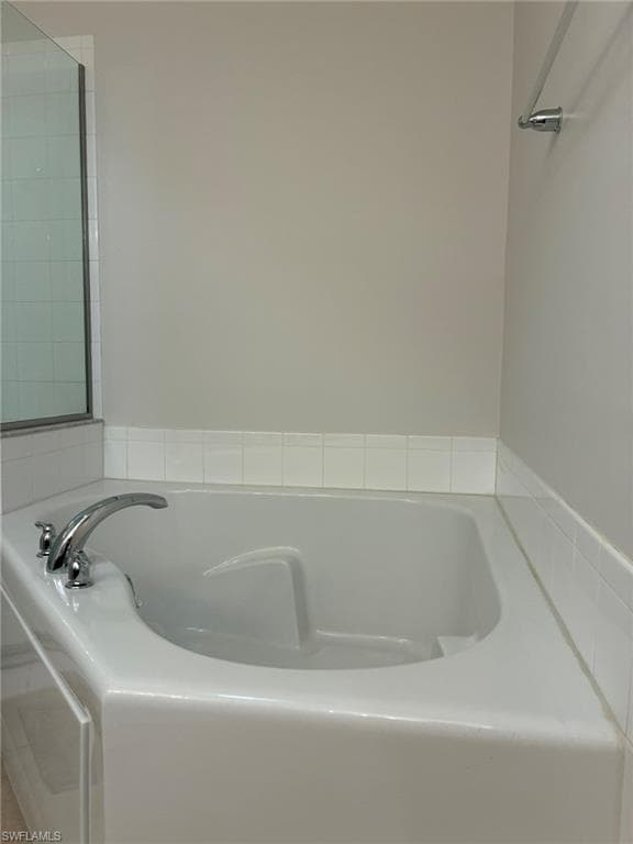 Corner soaking tub with chrome fixtures and surrounding white tile