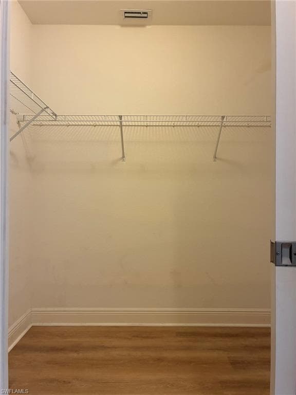 Interior storage closet featuring wood-finish flooring, white wire shelving, baseboard molding, and an overhead ventilation register