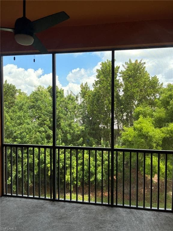 Screened porch with a textured concrete floor, black metal railing, and a ceiling fan with integrated lighting