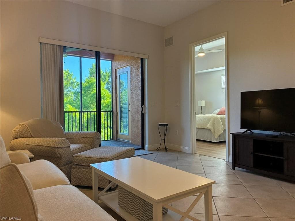 Living area featuring tile flooring throughout, direct balcony access through glass sliding doors, and a doorway opening to an additional room with wood-finish flooring and a ceiling fan