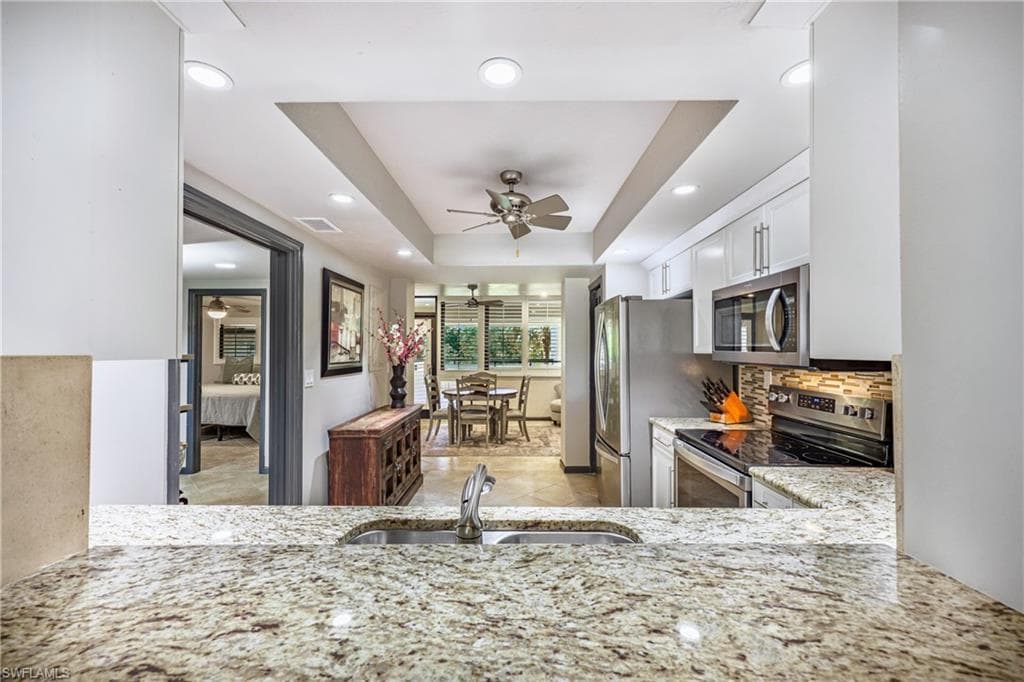 Kitchen featuring granite countertops, stainless steel appliances, white cabinetry, and a tile backsplash