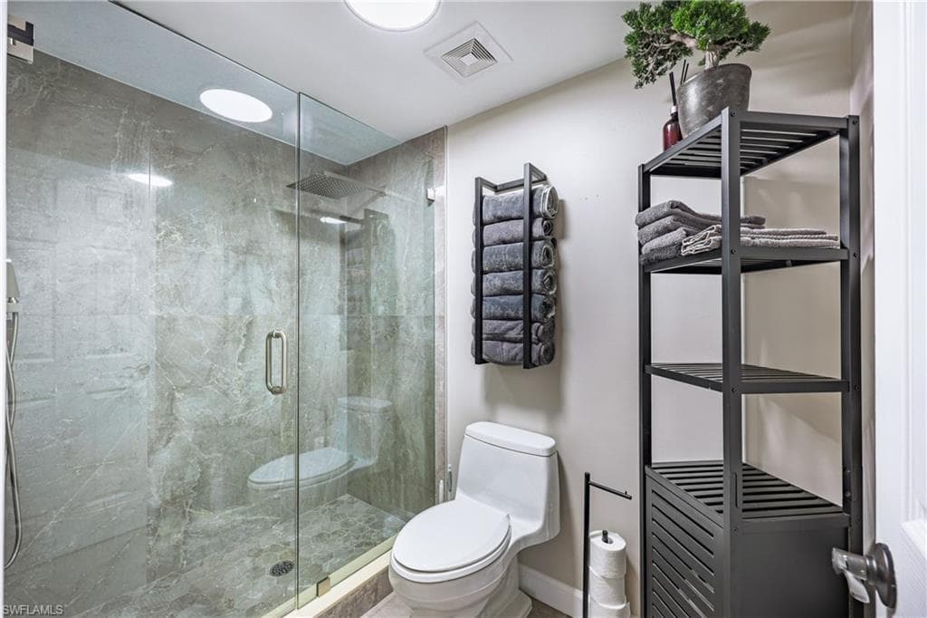 Full glass shower enclosure with floor-to-ceiling marble-look tile, a built-in shower niche, and a rain shower head