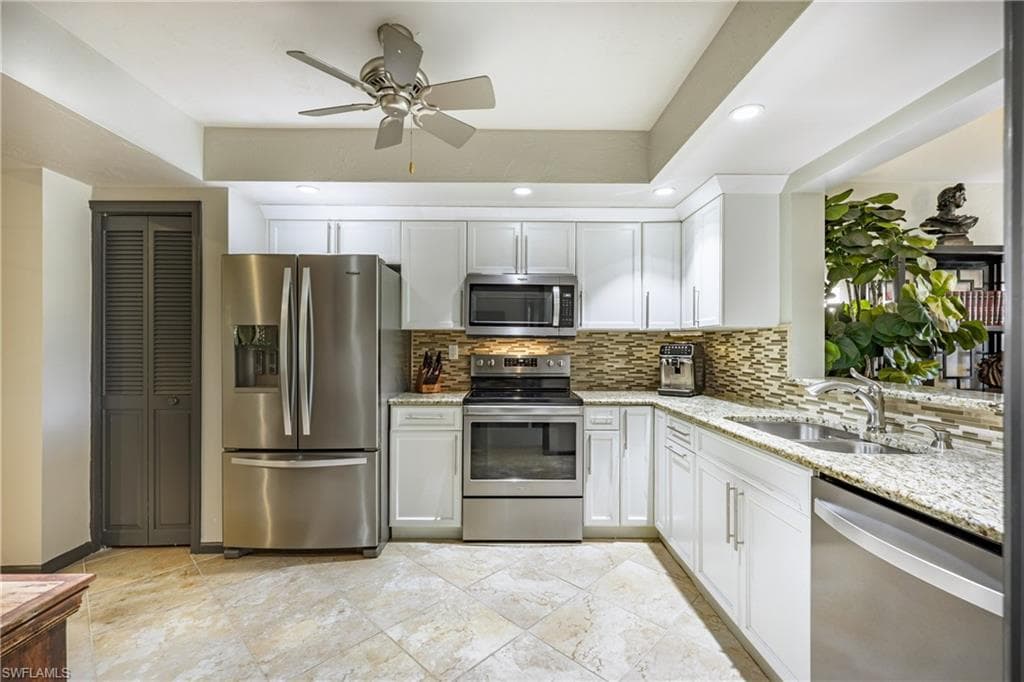 Kitchen featuring white cabinetry, stainless steel appliances, a multi-tone tile backsplash, and light-toned granite countertops