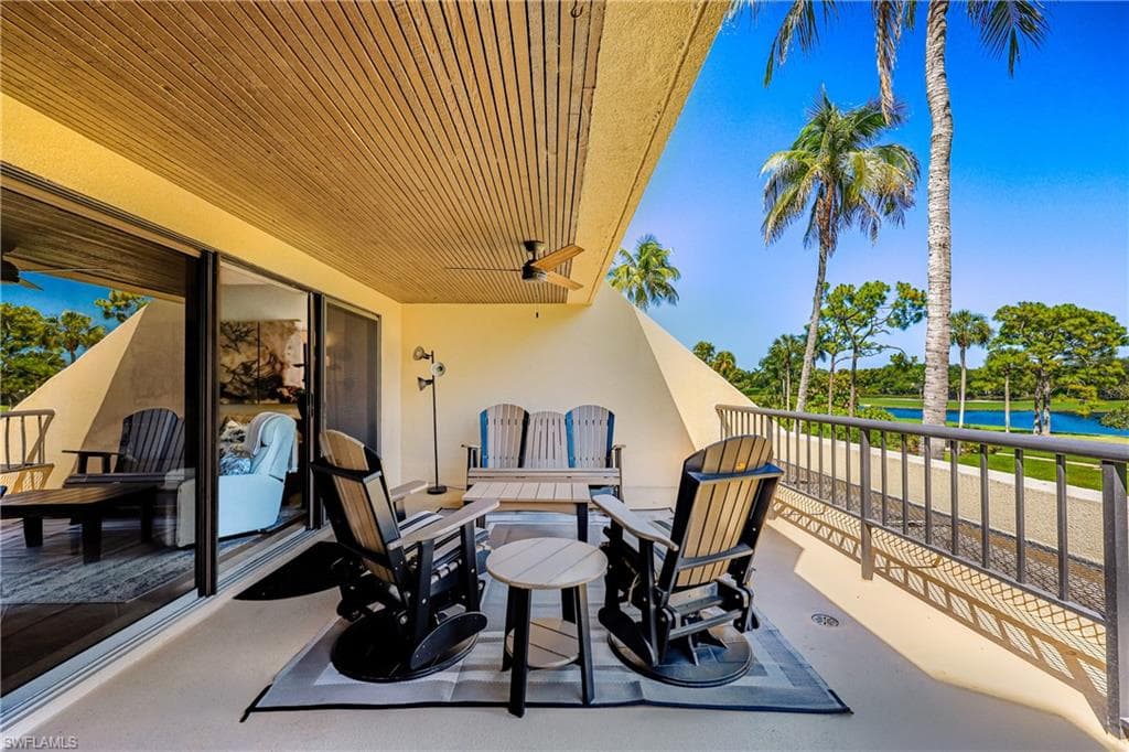 Expansive covered balcony featuring a slatted wood-finish ceiling, ceiling fan, and metal railing overlooking a body of water and lush landscaping