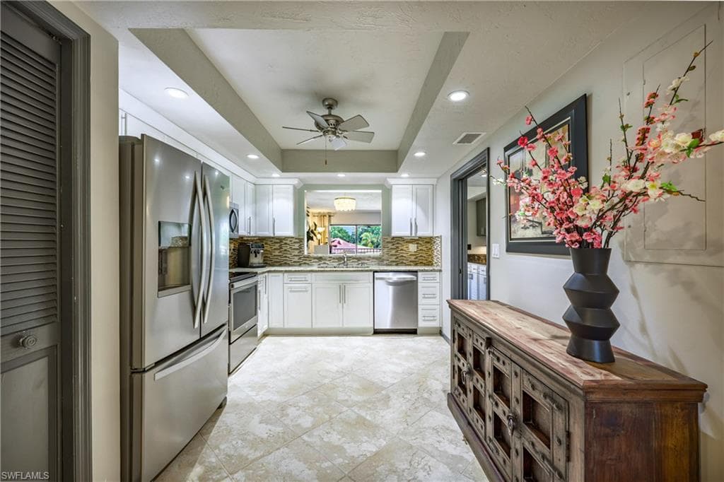 Kitchen featuring stainless steel appliances, white cabinetry, recessed lighting, and a tray ceiling with a ceiling fan