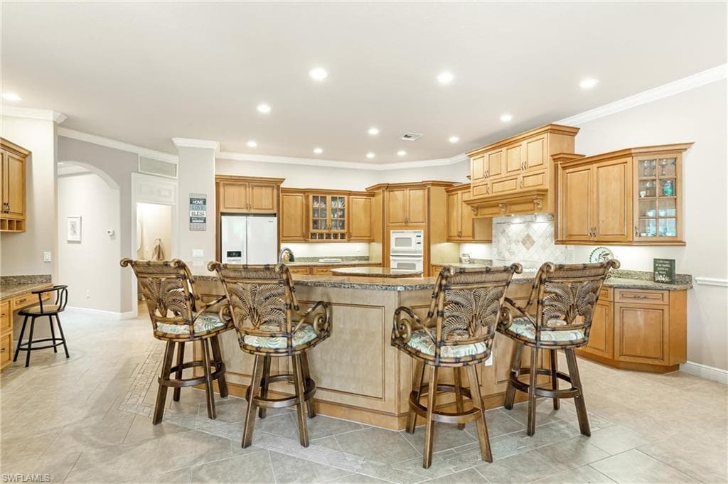 Spacious kitchen featuring breakfast bar, a large central island with seating, extensive wood cabinetry, light-toned countertops, tile backsplash, and recessed lighting