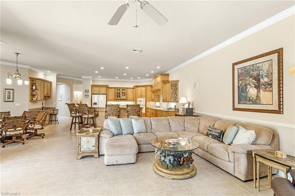 Expansive open-concept living area featuring light-toned tile flooring, recessed lighting, crown molding, and a ceiling fan