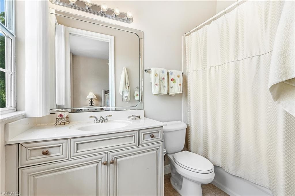 En-suite Bathroom featuring a single basin vanity with a light-colored countertop, an ornate framed mirror, and a shower/tub combination with a white curtain
