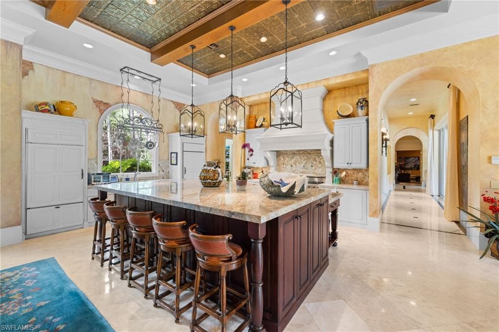 Expansive kitchen featuring a large central island with seating, a coffered ceiling with a pressed metal insert, and three decorative pendant lights