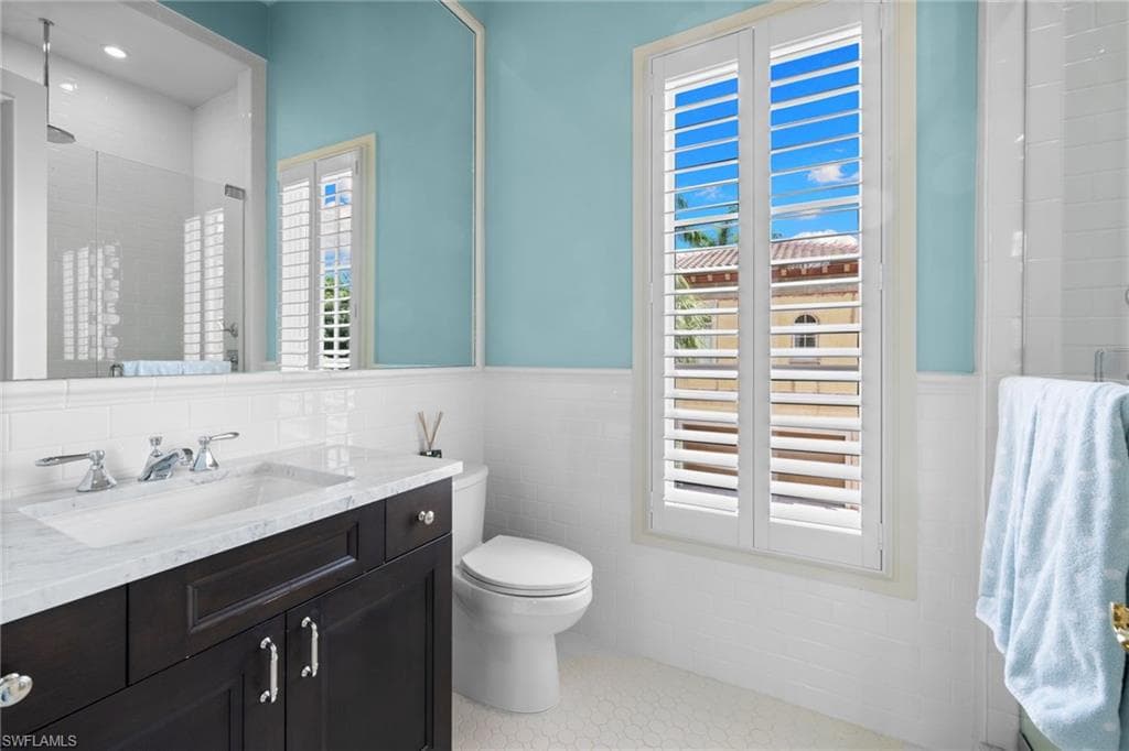 Bathroom featuring a dark wood vanity with a white countertop and integrated sink, chrome fixtures, white subway tile wainscoting, and plantation shutters