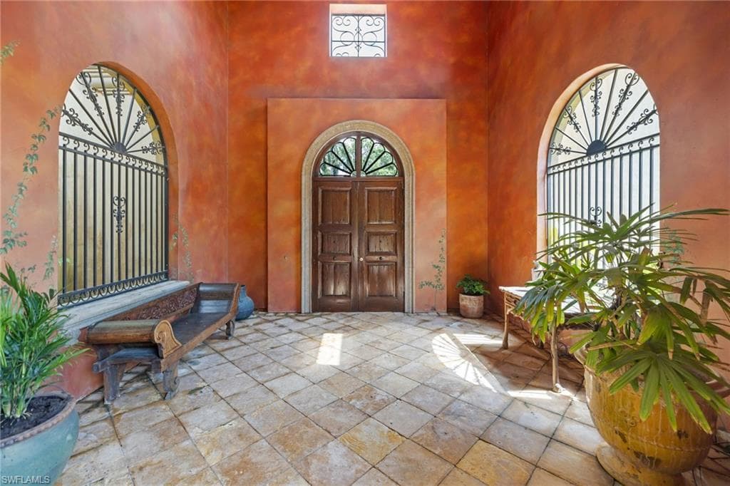 Arched entryway featuring a paneled wood door, stucco walls, wrought iron grilles, and square tile flooring