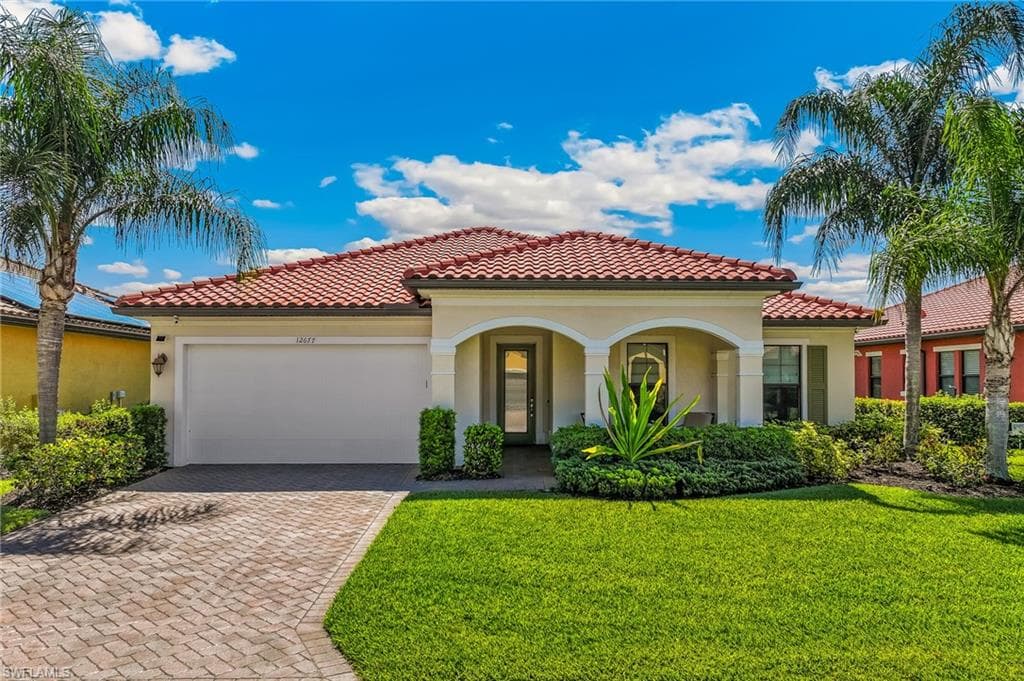 Mediterranean-inspired residence featuring a terracotta tile roof, arched entry portico, and a paver driveway