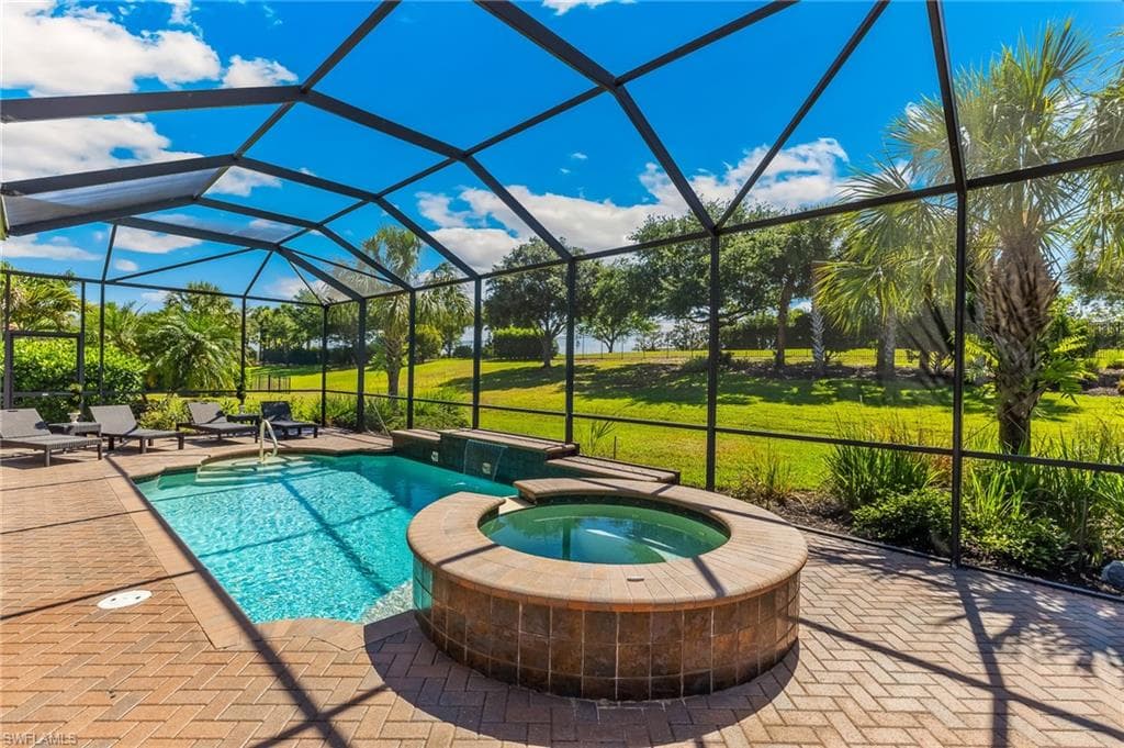 Screen-enclosed pool and spa area featuring brick paver decking, a rectangular pool with integrated steps, and a circular spa with tile surround
