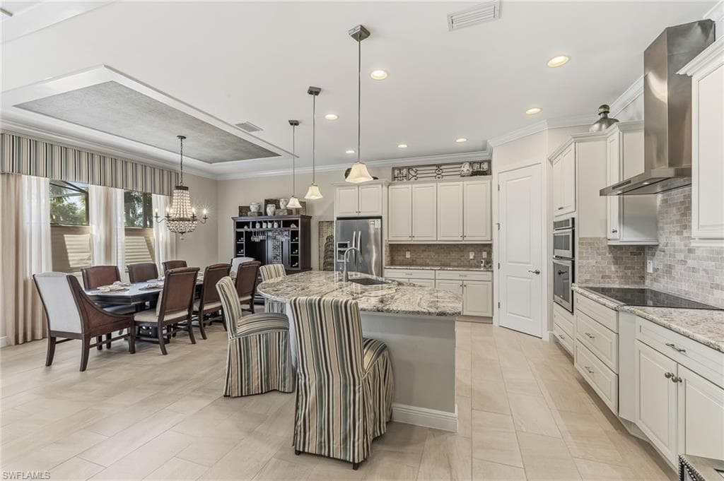 Spacious kitchen and dining area featuring light-toned tile flooring, recessed lighting, and a tray ceiling with a textured insert