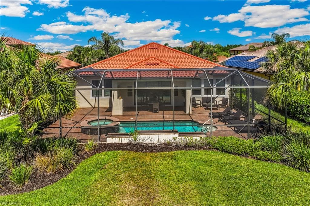 Rear exterior featuring a screened-in lanai with an integrated swimming pool and spa, a concrete patio, and a tiled roof