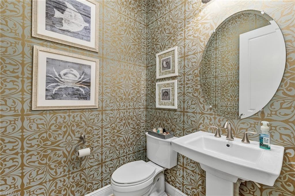 Pedestal sink with brushed nickel faucet, oval mirror, and patterned wallpaper