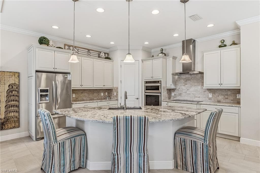 Gourmet kitchen featuring a curved island with stone countertops, stainless steel appliances, white cabinetry, and a tile backsplash