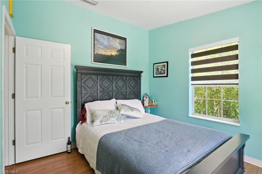 Spacious room featuring a white paneled door, wood-finish flooring, and a window with horizontal blinds