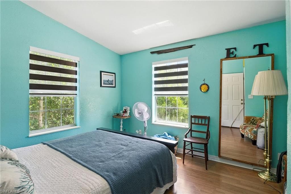Room featuring wood-finish flooring, two windows with horizontal blinds, and a built-in shelf