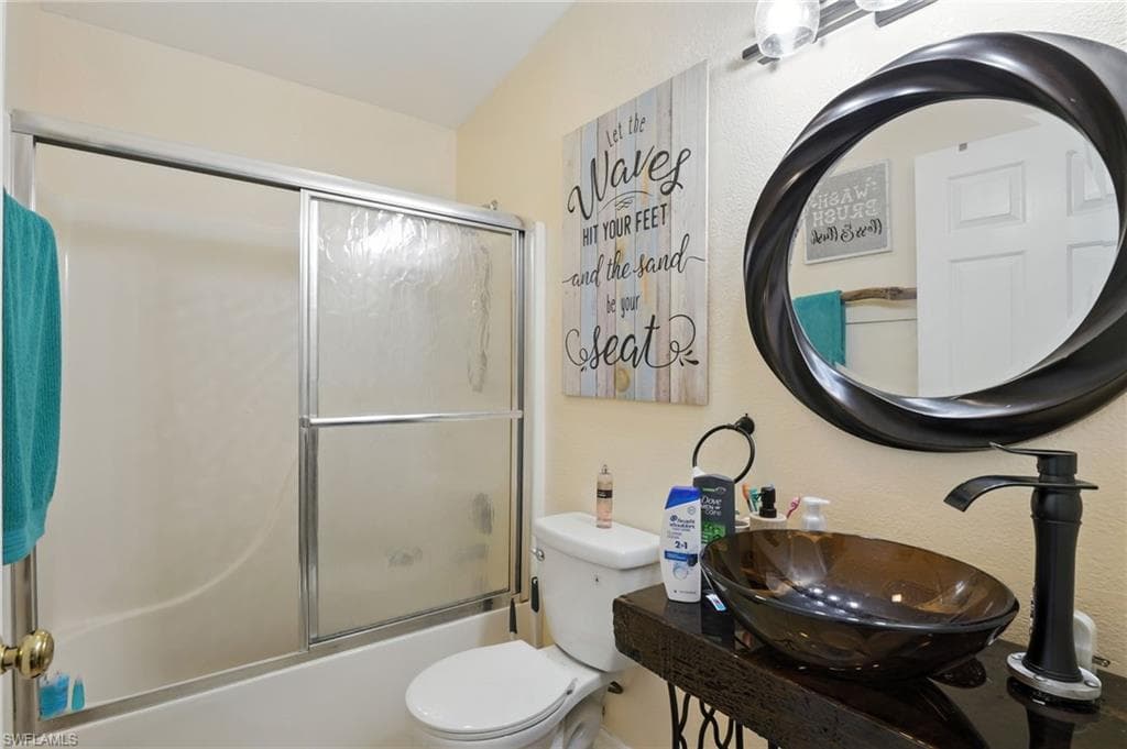 Bathroom featuring a tub/shower combination with sliding glass doors, a modern vanity with a vessel sink, and a circular mirror with a decorative frame