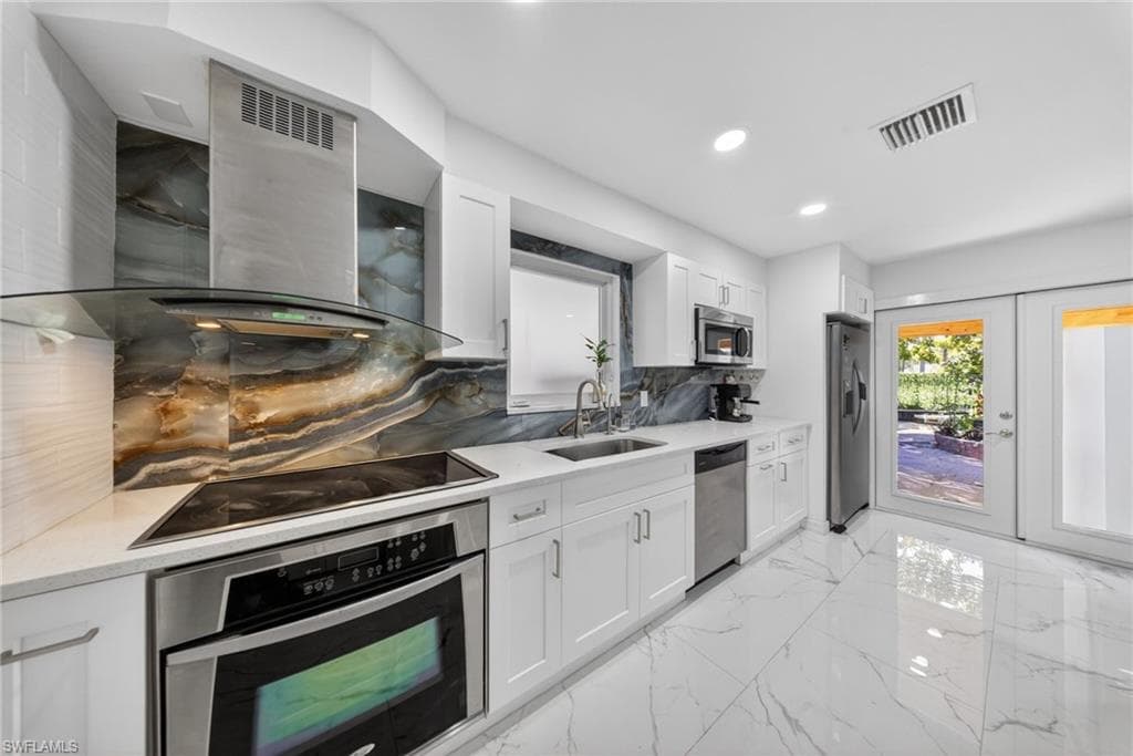 Contemporary kitchen featuring a striking stone slab backsplash, sleek white cabinetry, stainless steel appliances, white countertops, and expansive large-format tile flooring