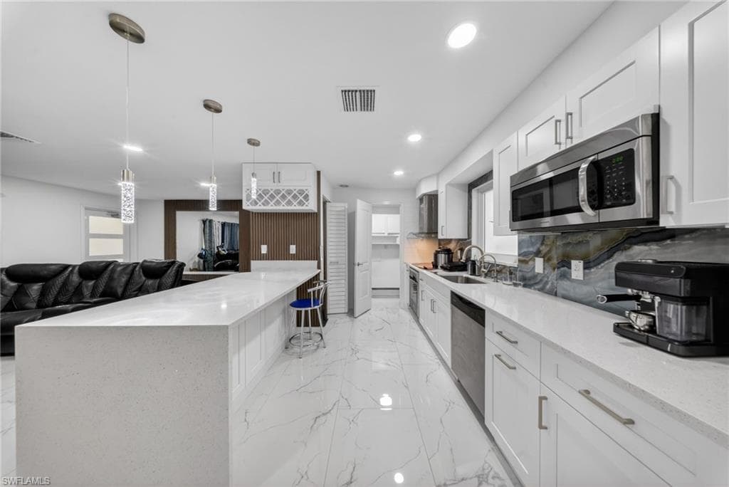 Open-concept kitchen featuring an expansive island with a waterfall edge, white shaker cabinetry, stainless steel appliances, a unique backsplash, and polished porcelain flooring