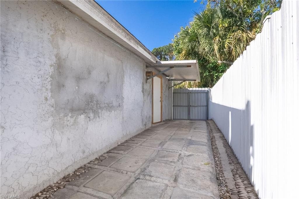 Concrete paver pathway with gravel edging, bordered by a textured stucco wall and a white corrugated fence