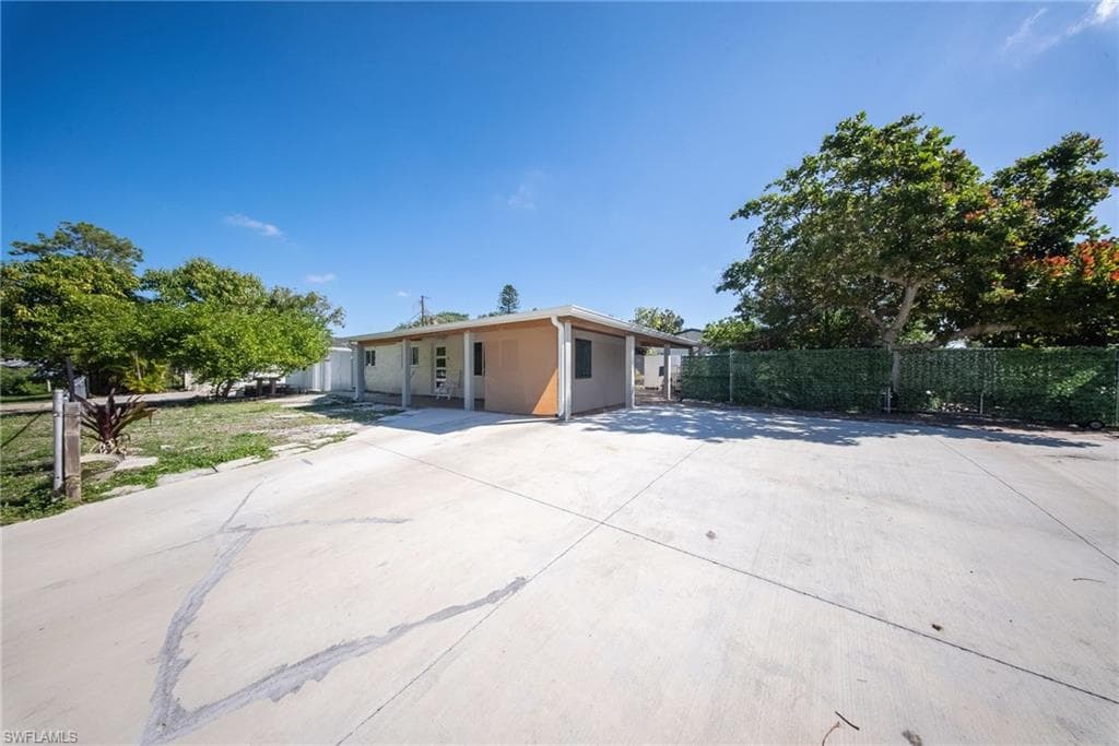 Spacious concrete driveway with mature trees and a privacy hedge outlining the property perimeter