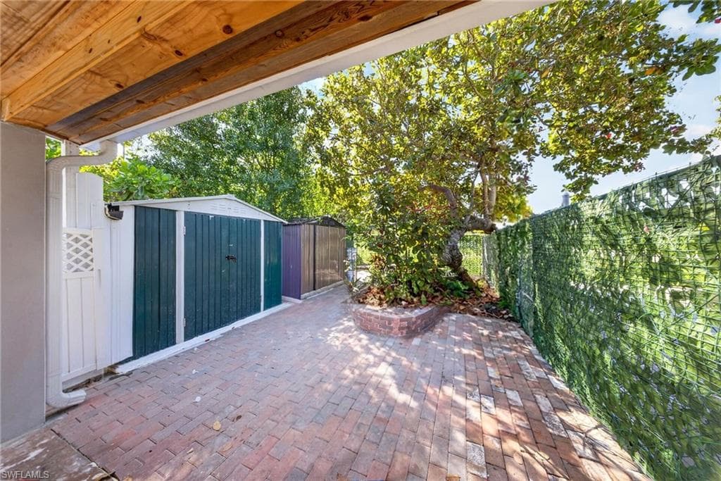 Brick paver patio area featuring a mature tree, an attached trellis with greenery, and multiple storage sheds