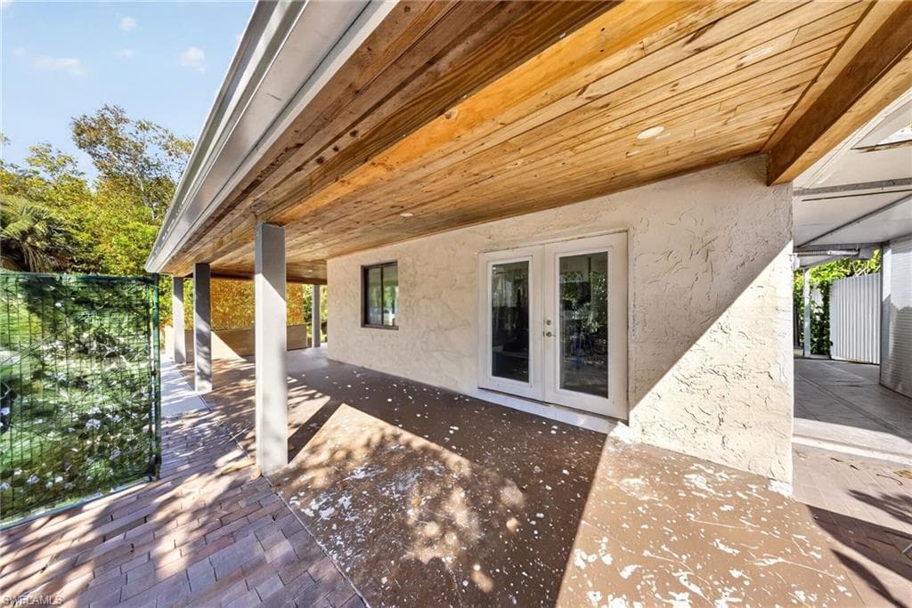 Covered patio featuring a wood-finish ceiling, textured exterior wall, and white frame French doors