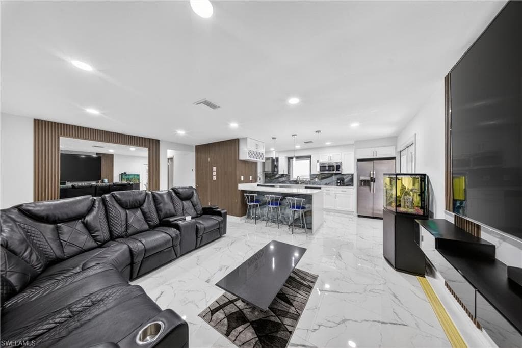 Open-concept living space featuring white marble-look flooring, recessed lighting, and a kitchen island with seating