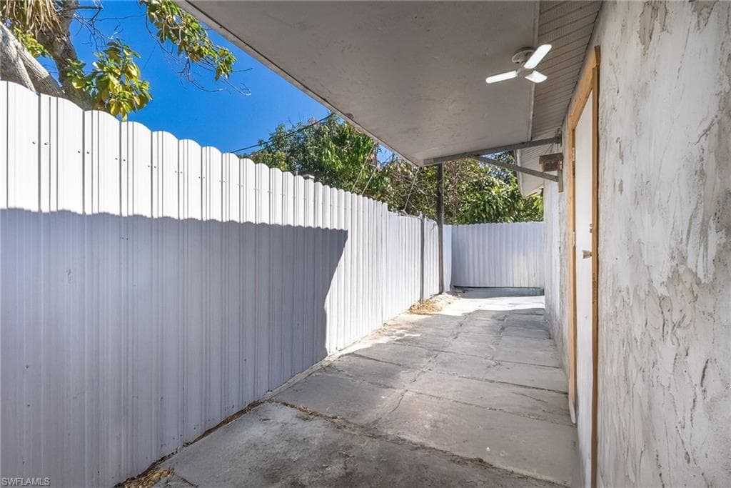 Covered side walkway featuring a textured exterior wall, concrete flooring, and a white corrugated metal fence